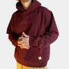 A person wearing a burgundy Shakahs hoodie with the brand's logo embroidered on the front and the sleeve.